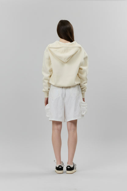 Person wearing a cream-colored hoodie and white shorts on a gray background