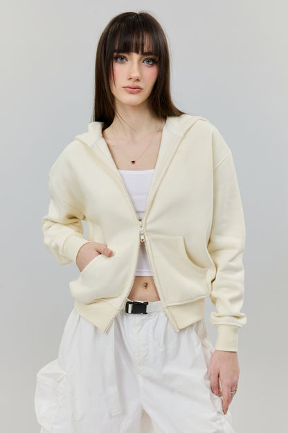 Woman wearing a light beige cardigan over a white top and pants on a plain background