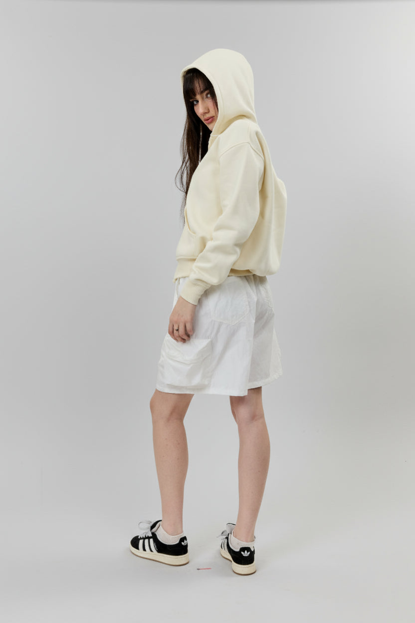 Person wearing a cream hoodie and white shorts on a plain background