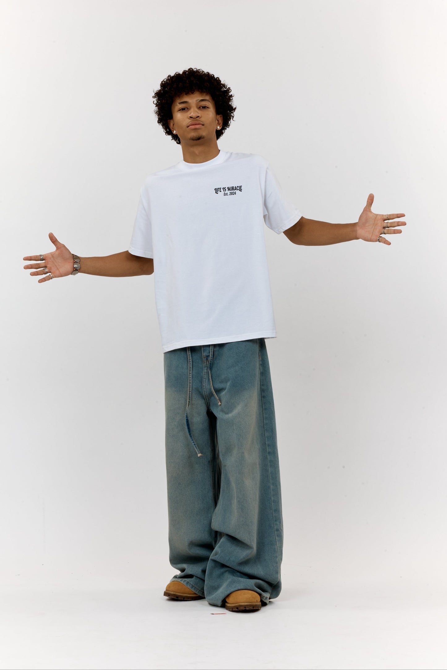 Person wearing a white t-shirt and blue jeans standing with arms outstretched on a white background