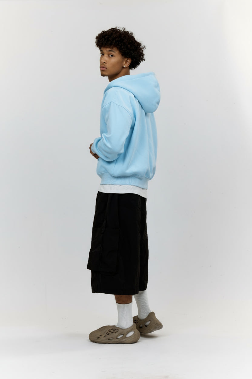 Person wearing a light blue hoodie, black pants, and white socks on a white background