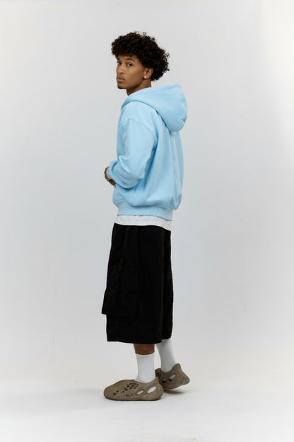 Person wearing a light blue hoodie, black pants, and white socks on a white background