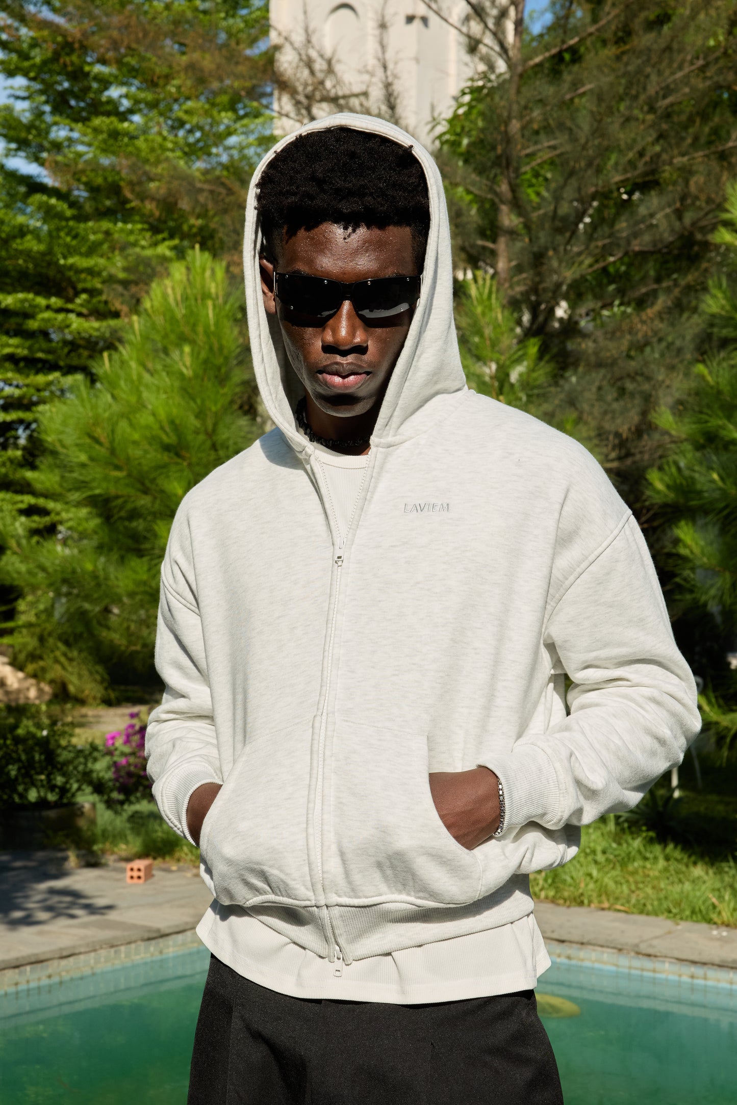 Person wearing a white hoodie with a brand logo, standing outdoors near a pool.