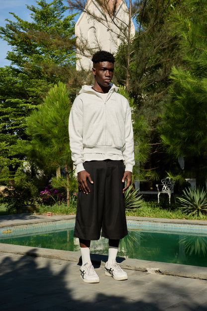 Man wearing a white hoodie and black pants standing by a pool with greenery in the background