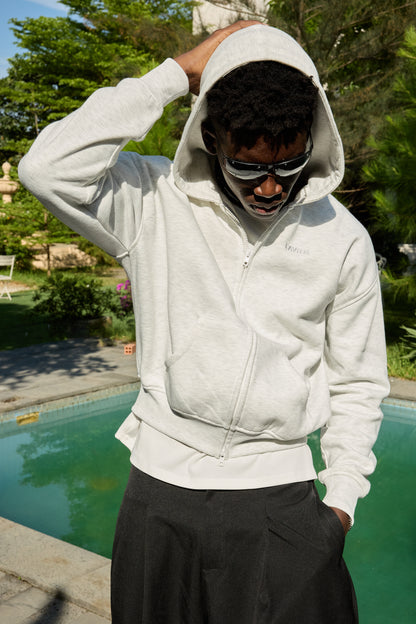 Person wearing a white hoodie and sunglasses by a pool with greenery in the background