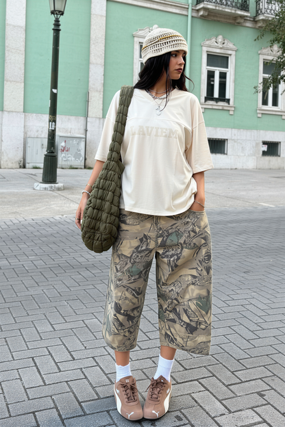 Person wearing a white shirt, camouflage pants, and a knit hat on a street.