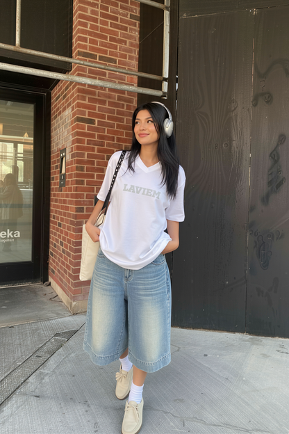 Woman wearing a white t-shirt and blue jeans standing on a sidewalk.