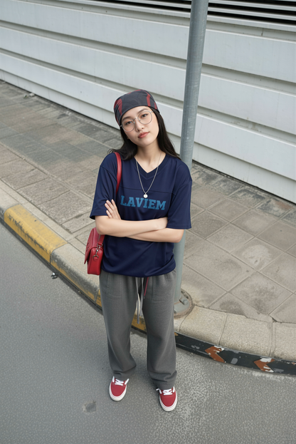 Person wearing a blue 'LAVIEM' t-shirt with gray pants and red shoes, standing on a sidewalk.