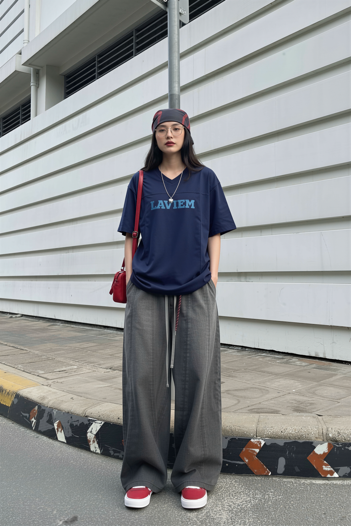 Person wearing a navy blue t-shirt with 'LAVIEM' text, gray wide-leg pants, and red shoes, standing against a white wall.