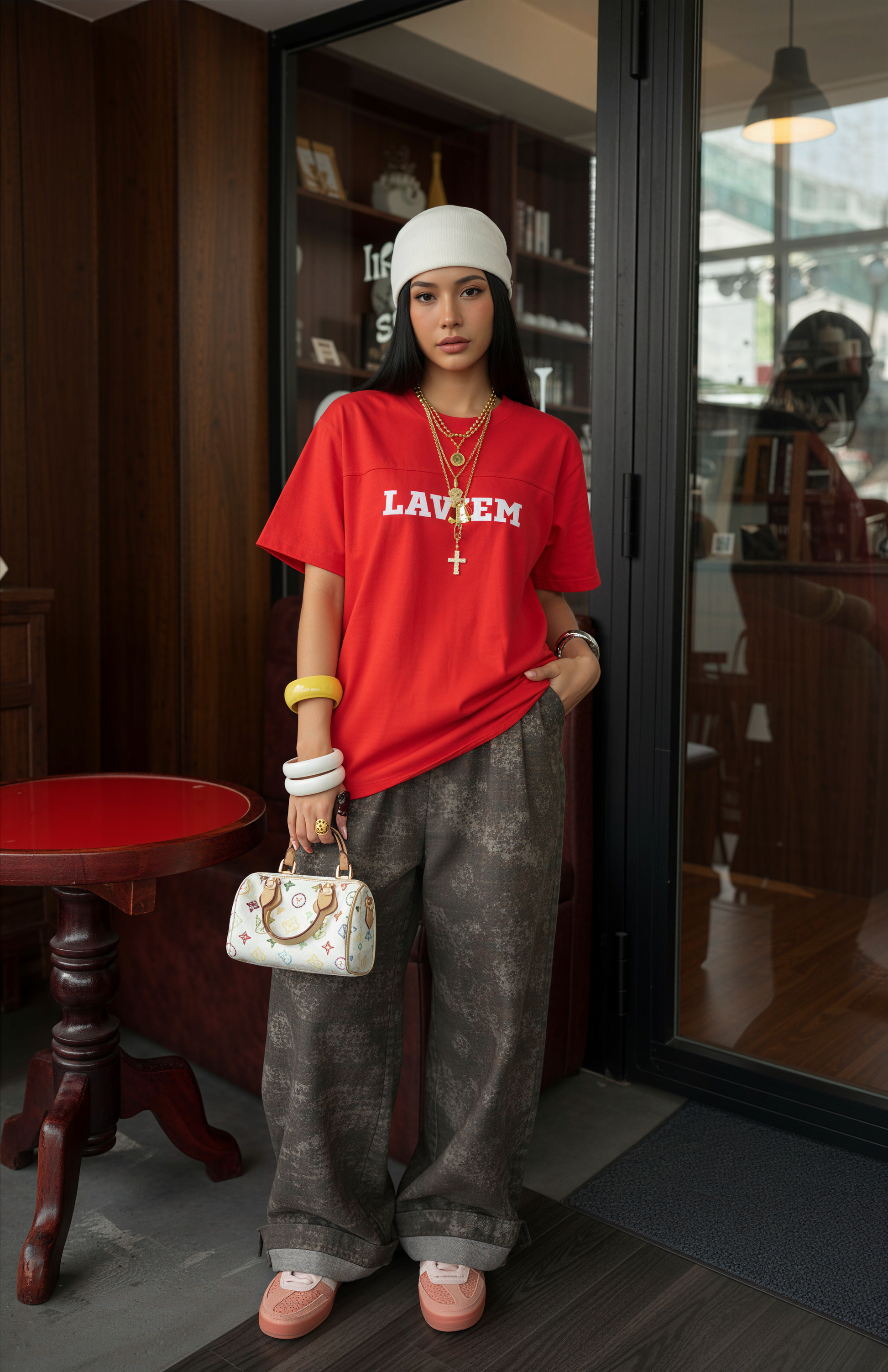 Person wearing a red t-shirt with text, gray pants, and white shoes indoors.