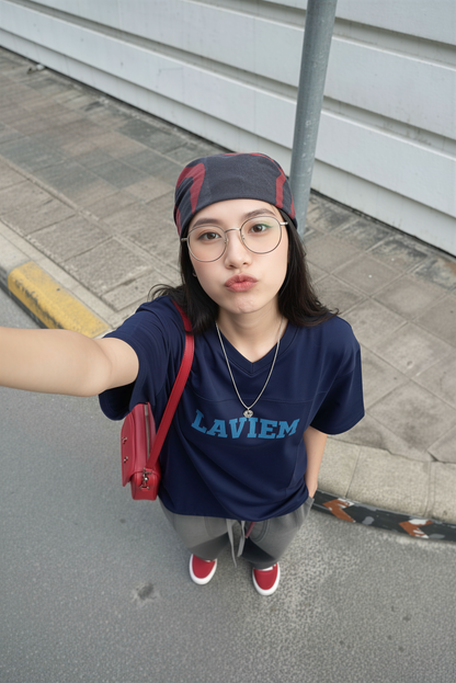 Person wearing a blue shirt with 'LAVIEM' text, red bag, and headband on a sidewalk.